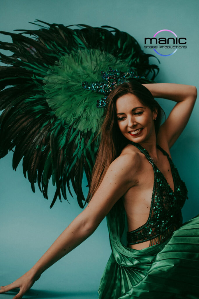 Green goddess showgirl posing for the camera with large feathered headdress and sequin leotard on