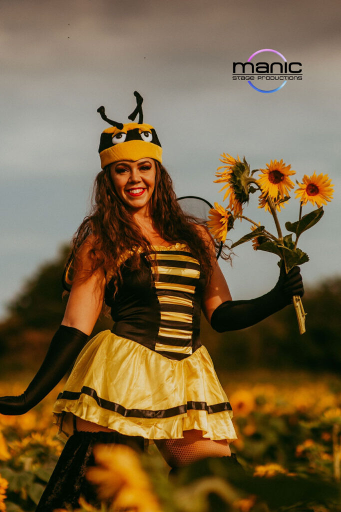 Stilt walking bumble bee holding sunflowers in her had whilst walking through a sunflower field on Hayling Island