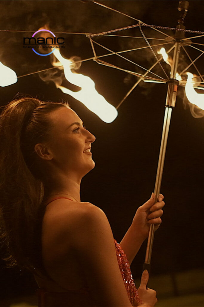 Fire umbrella dancer holding a burning umbrella above her head in the dark night sky