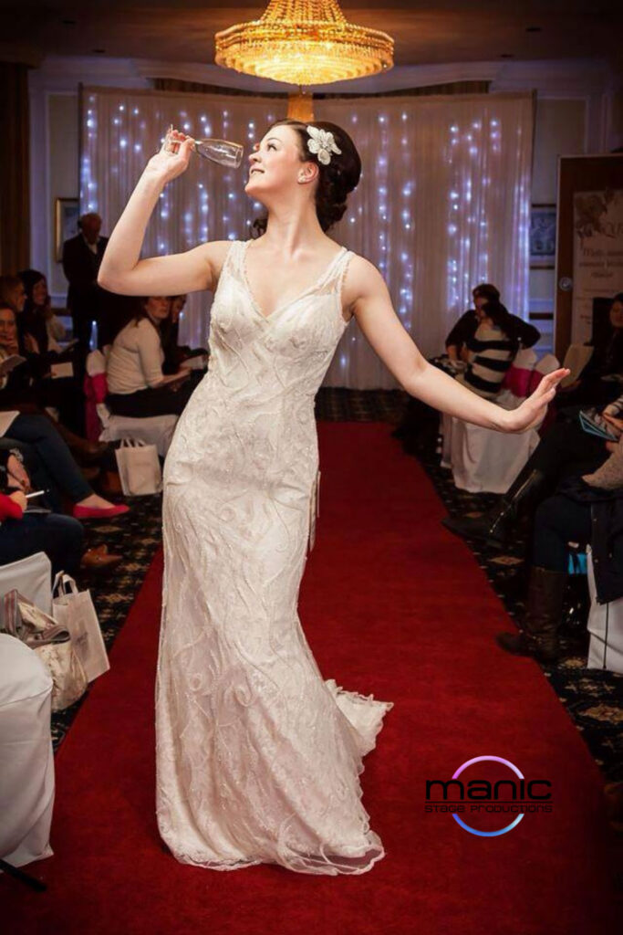 Bridal model walking down the red carpeted catwalk with a glass of champagne