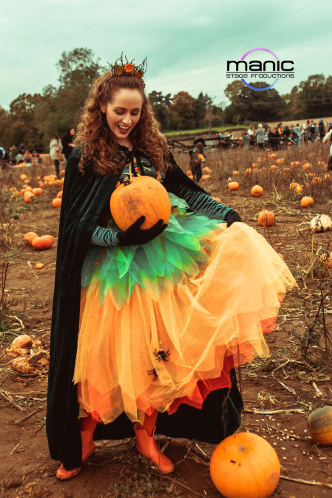 Pumpkin princess actress holding a large orange pumpkin in a muddy field at Rowgate pumpkin patch