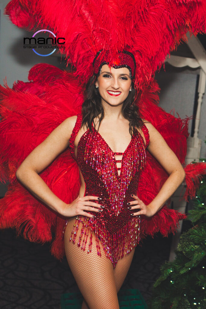 Red Christmas showgirl meet and greet hostess stood smiking nec=xt to a Christmas tree welcoming party guests