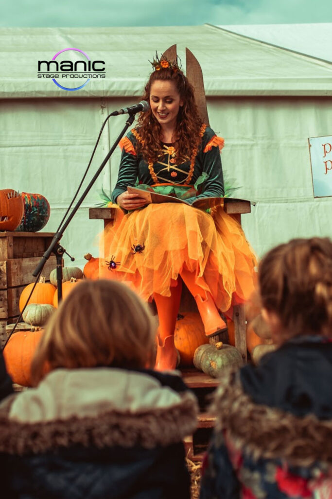 Pumpkin princess actress sat reading a story to children listening on hay bales at a halloween event
