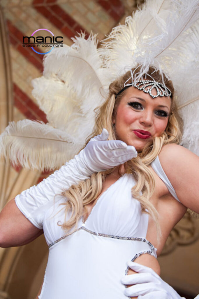 White feathered showgirl blowing a kiss to the camera wearing white gloves and a diamond headdress